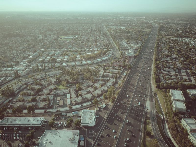 High-altitude drone shot capturing a busy freeway running alongside a suburban town during the day.