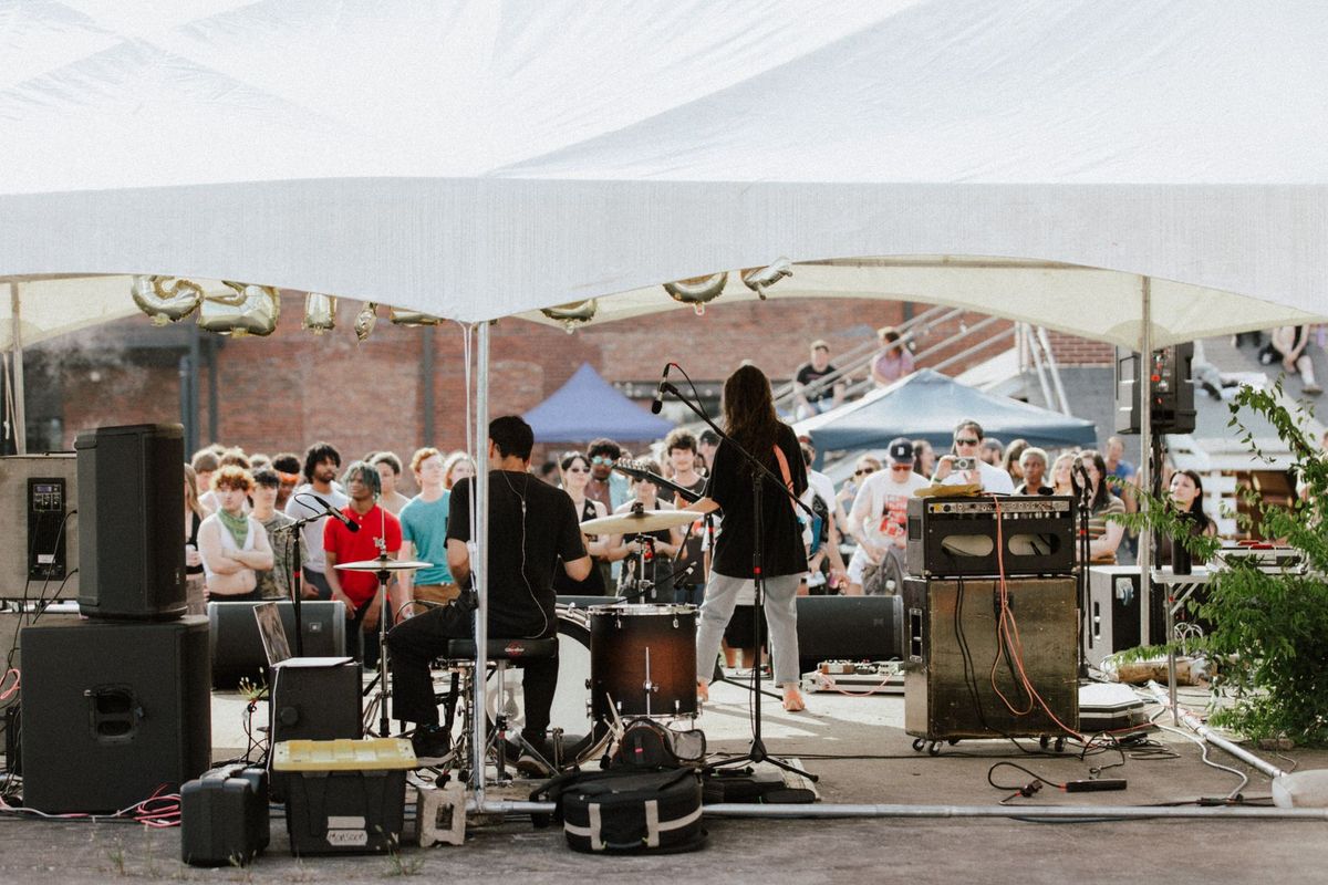 A lively outdoor band performance with an energetic crowd enjoying live music under a tent.