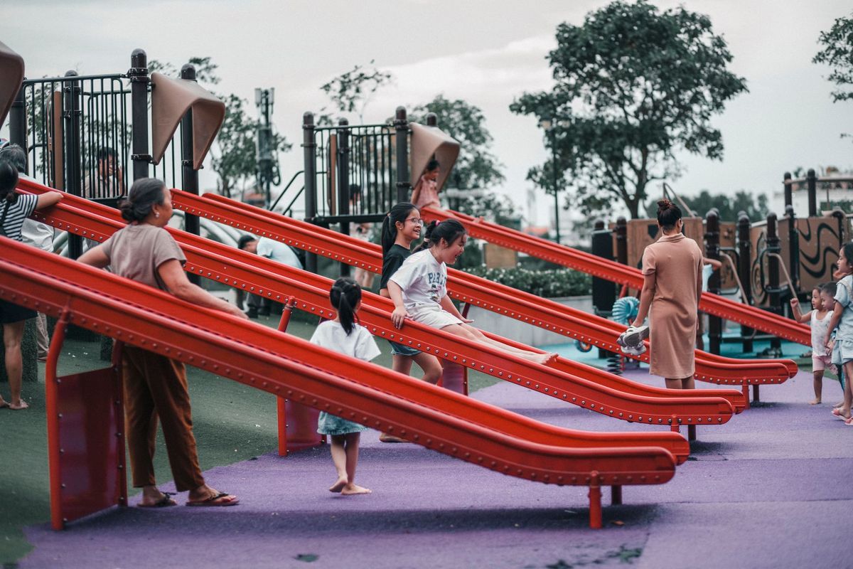 Group of children and adults enjoying a sunny day at a colorful outdoor playground with slides.
